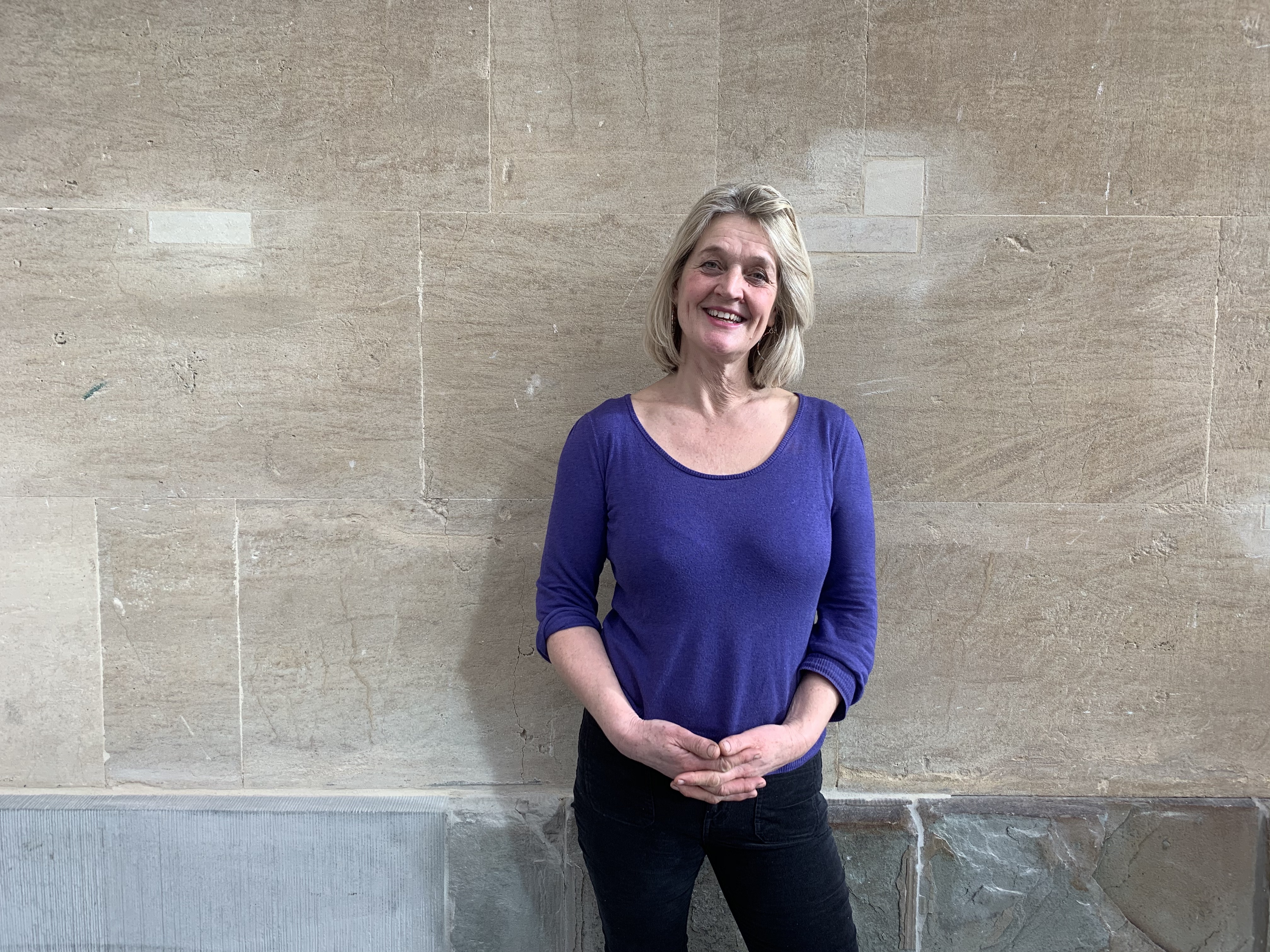 A portrait of Kate Gedge, a lady with blonde short shoulder length hair wearing a bright blue jumper 