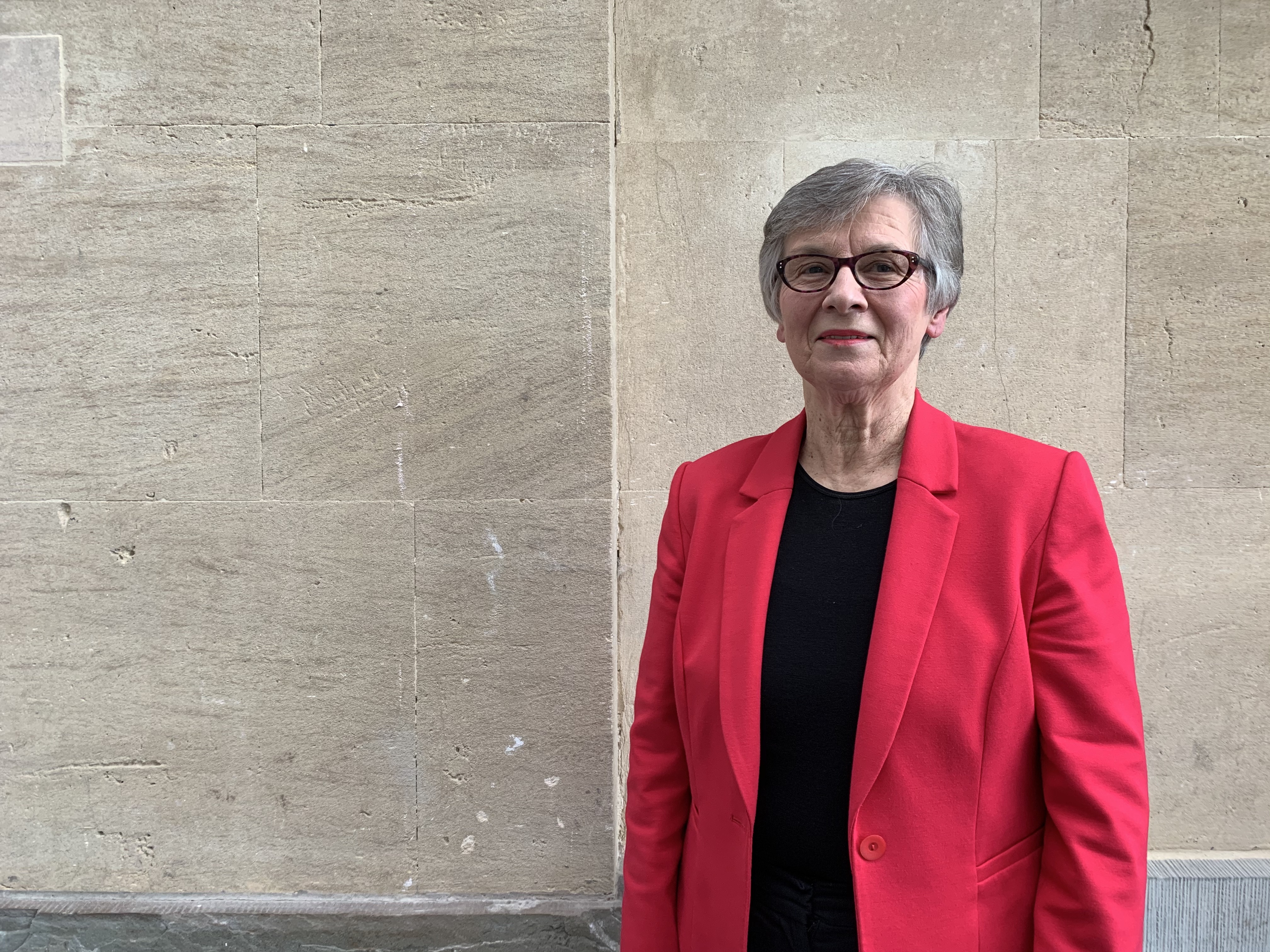 Portrait of Elizabeth Jeffreys, who has short cropped hair and glasses and is wearing a red blazer and black top