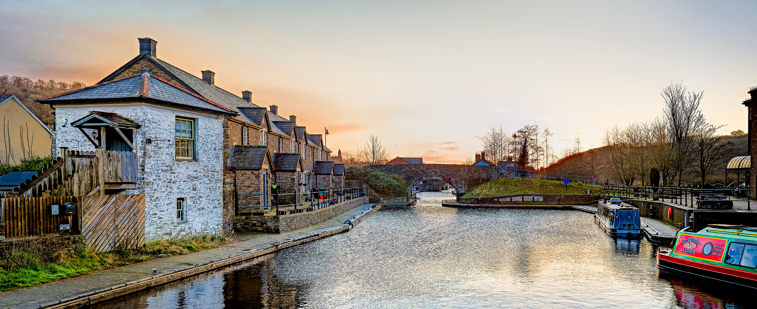 Image of Brecon canal with a colourful long boat in the foreground and a row of welsh cottages in the background