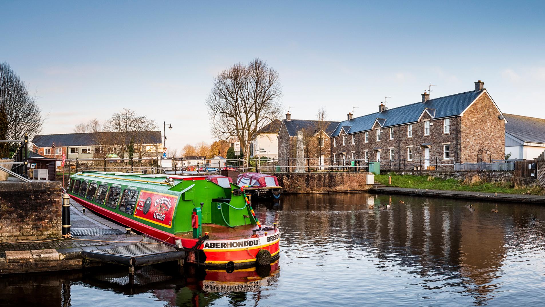 Image of Brecon canal with a colourful long boat in the foreground and a row of welsh cottages in the background